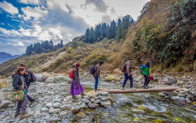 Hikers crossing wooden bridge over mountain stream in Rajgundha trek