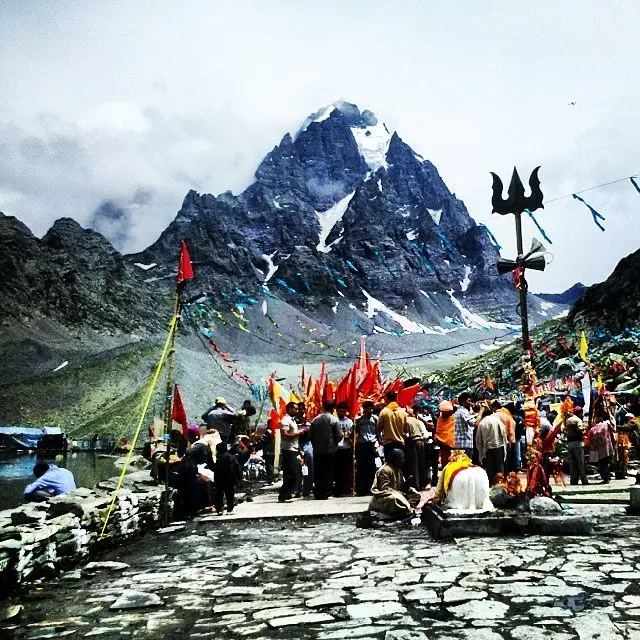 Snow‑capped Manimahesh Kailash peak towering behind pilgrim tents - Mountain Junkey