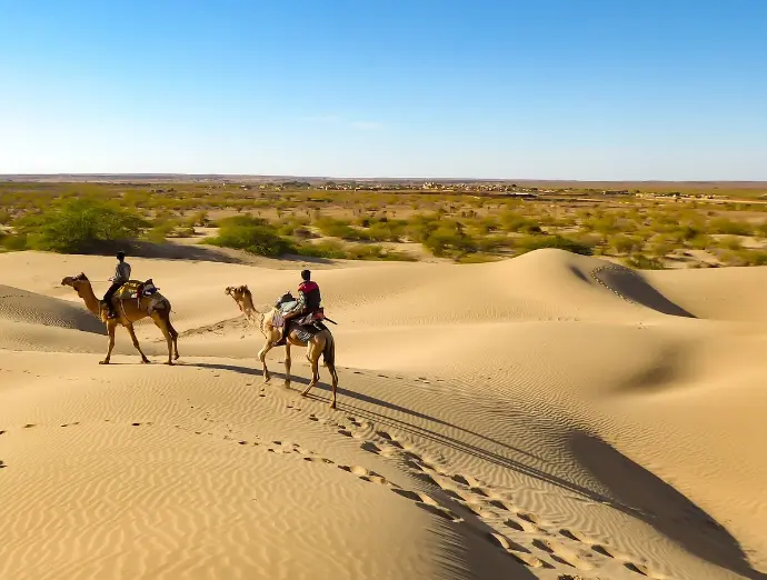 Camel riders crossing sand dunes in Thar Desert, authentic Rajasthan scene - Mountain Junkey